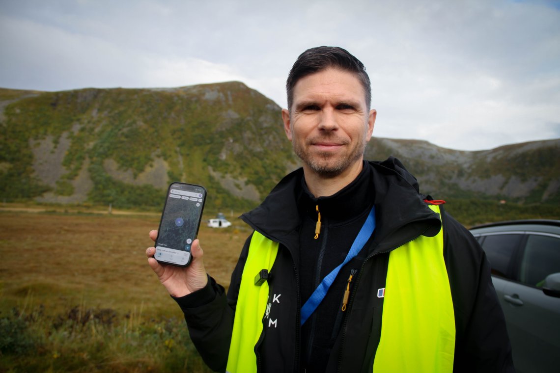 Espen Slette står med gul refleksvest og holder opp telefonen sin hvor han er inne på Google Maps