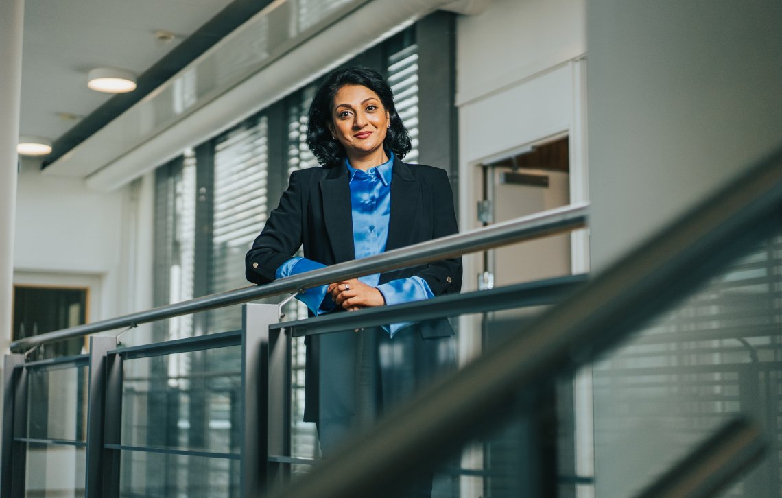 Avdelingsdirektør Kamilla i Sharma står ved et gelender i et glassbygg.
