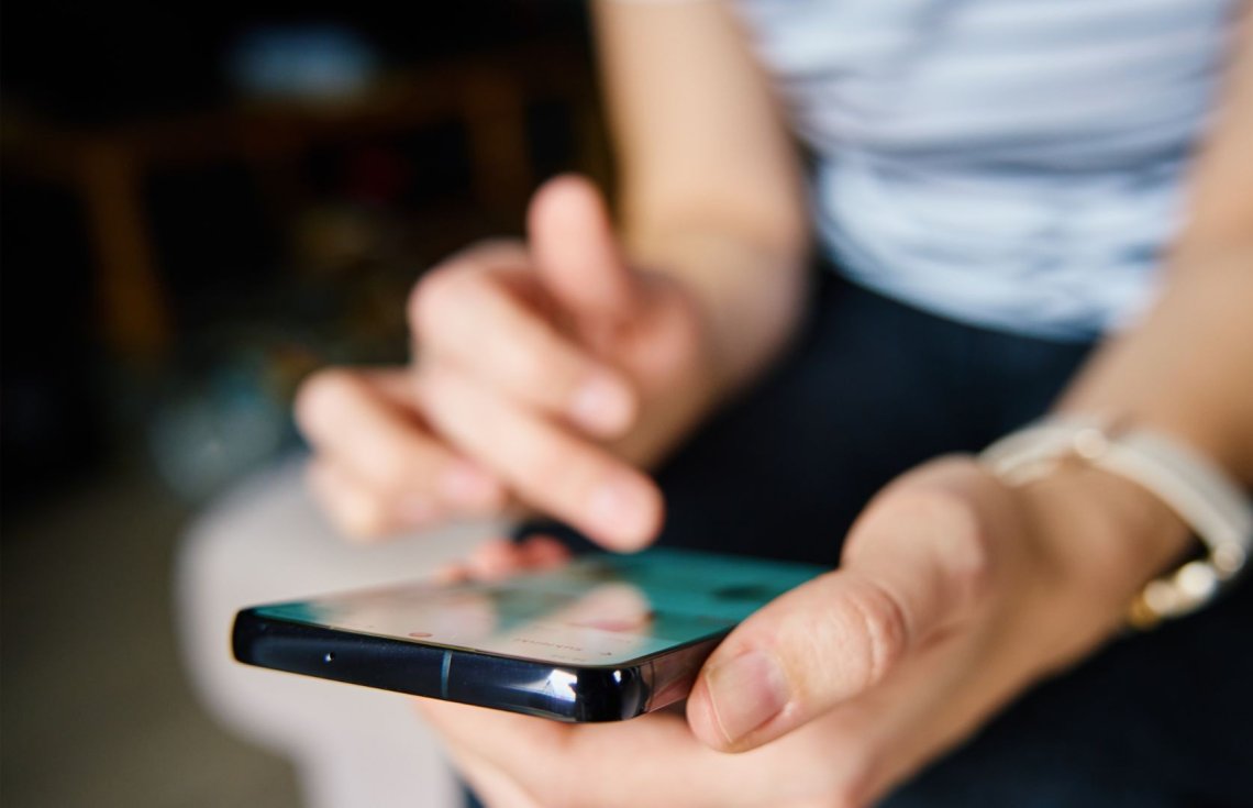 Bildet viser nærbildet av to hender hvor en holder en telefon og den andre trykker på telefonen. 