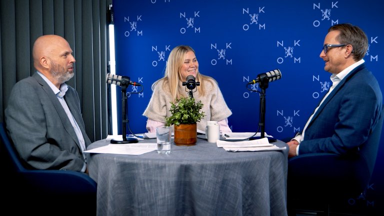 Tre personer sitter rundt et rundbord med mikrofoner foran seg i et studio med Nkom‑bakgrunn