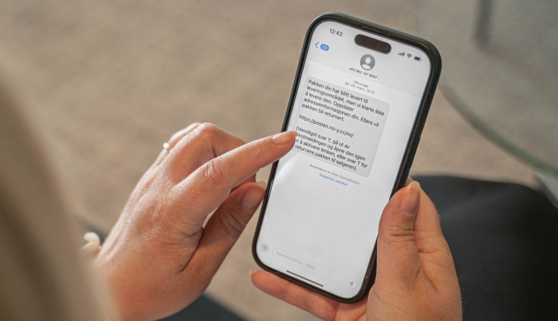 Hånd som holder en telefon med en falsk tekstmelding fra Posten